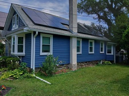 Blue house with solar panels on the roof, green lawn, white trim, and a chimney.