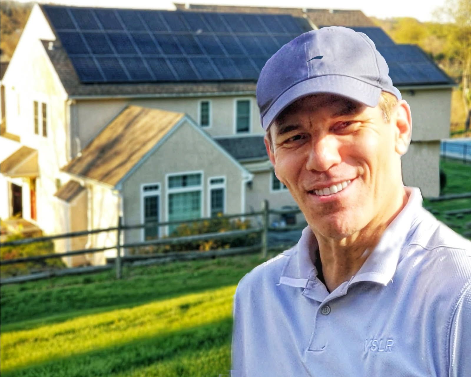 Large angled solar panel array on a grassy hillside, in front of a building and trees.