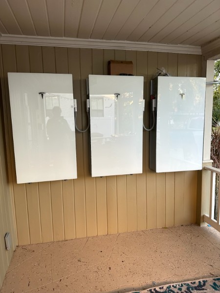 Exterior electrical equipment mounted on a blue house with surrounding greenery; hibiscus flower in bloom.
