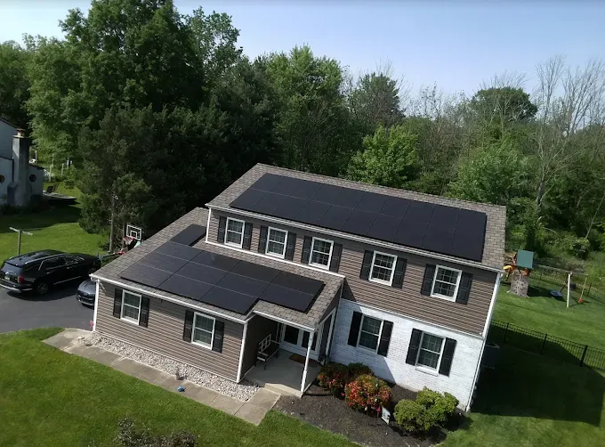 Solar panels on a two-story house with brown siding and a green lawn.