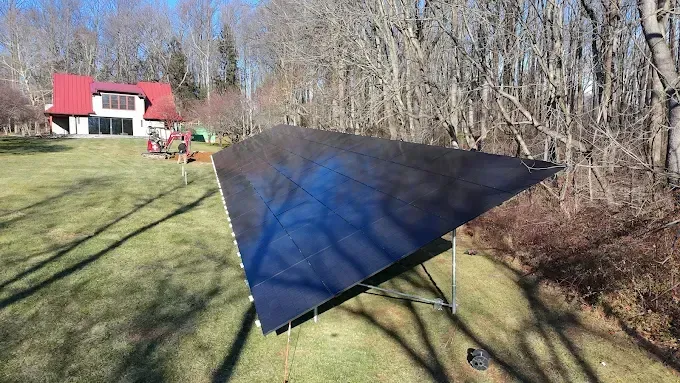 Large solar panel array in a grassy yard, house and trees in the background. Sunny day.