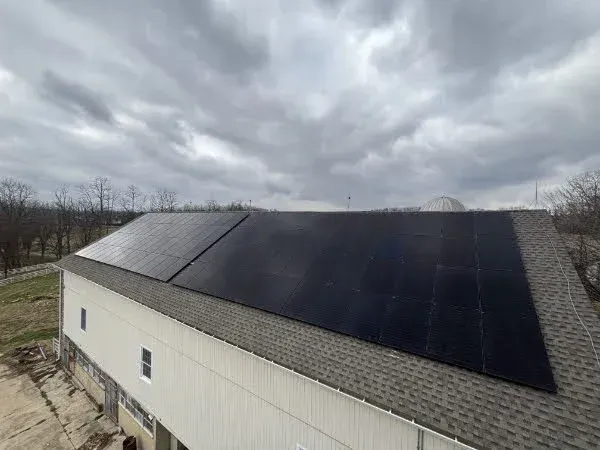 Solar panels installed on a white building's roof under a cloudy sky.