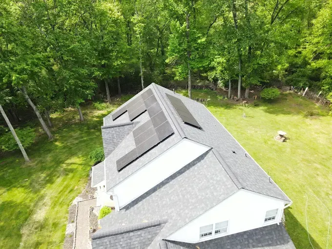 Solar panels installed on a gray roof, surrounded by green trees and grass.