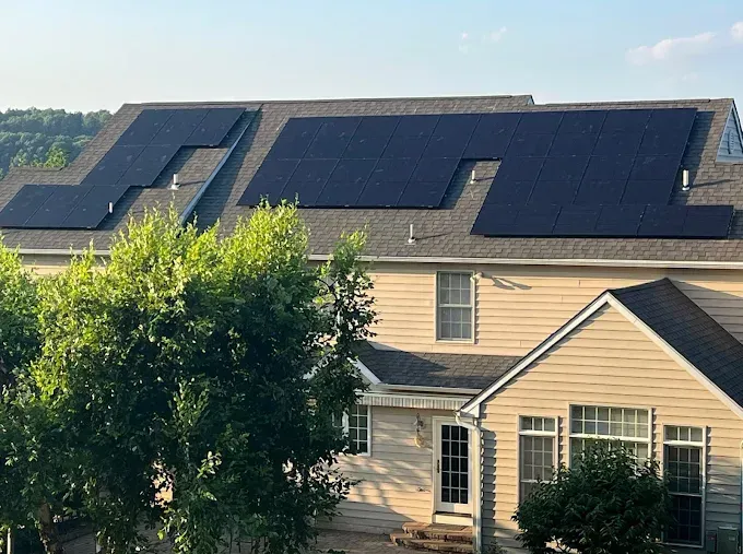 Solar panels on a house roof. Dark panels on a beige-colored house with green trees in the foreground.