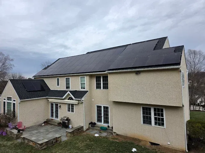 Solar panels installed on the roof of a beige house under a cloudy sky.