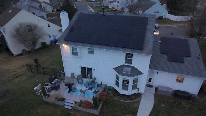 Aerial view of a white house with solar panels on the roof and a patio with people sitting around.