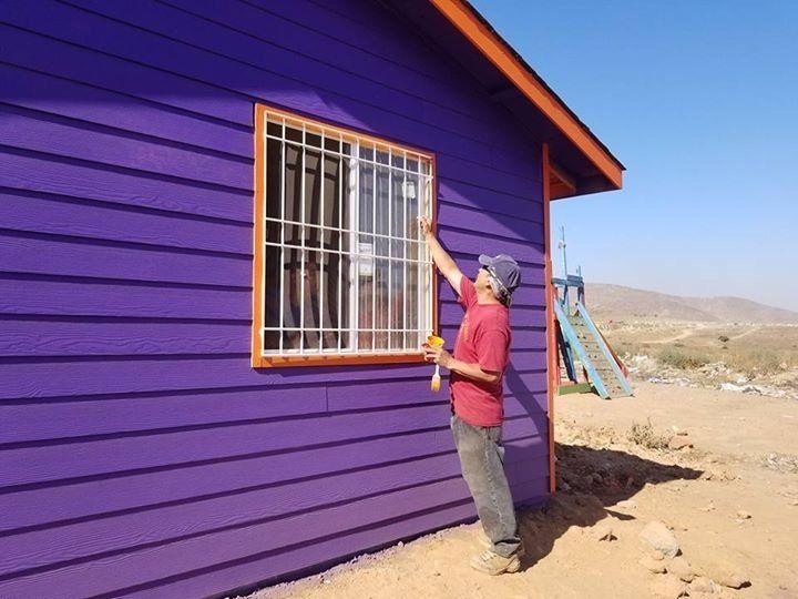 A man paints a window on a purple house