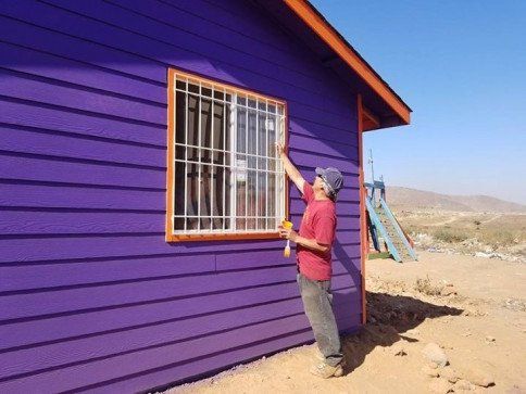 A man paints a window on a purple house