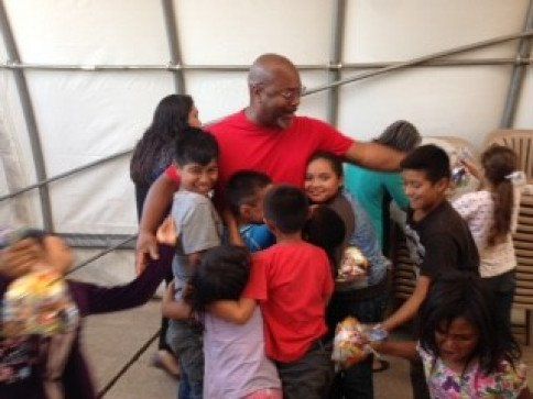 A man in a red shirt is hugging a group of children.