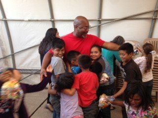 A man in a red shirt is hugging a group of children.