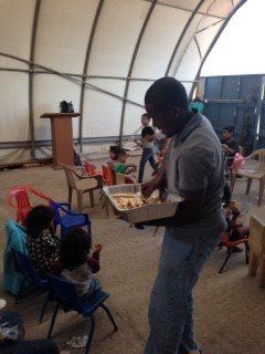 A man is holding a tray of food in front of a group of children