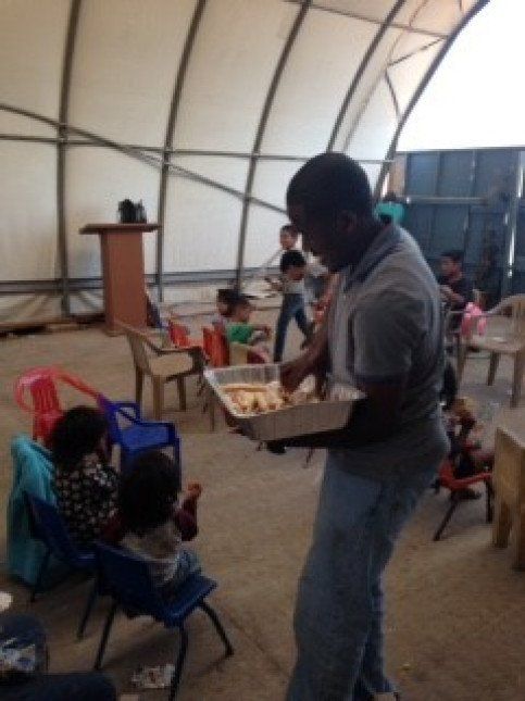 A man is holding a tray of food in front of a group of children