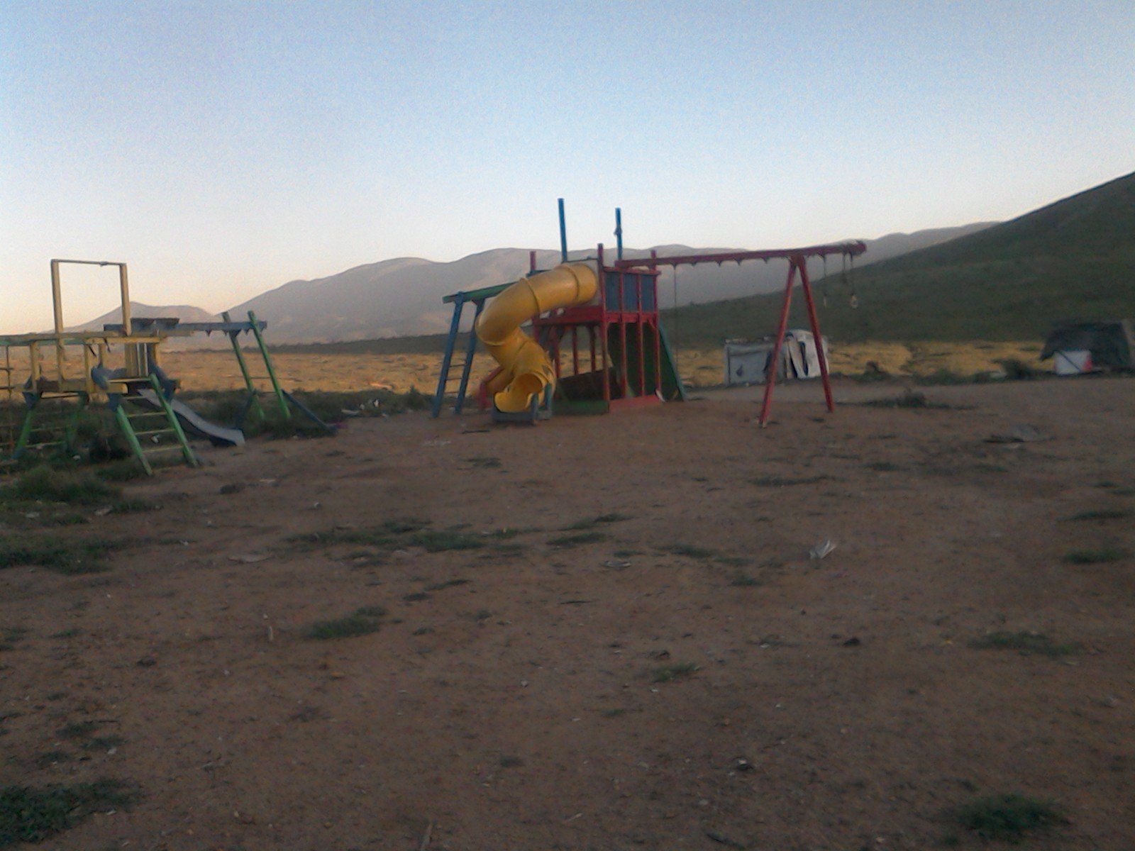 A playground with mountains in the background and a yellow slide
