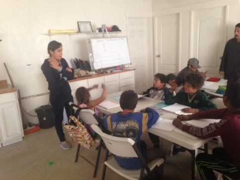 A woman is standing in front of a group of children in a classroom.