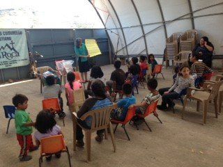 A group of children are sitting in chairs in front of a sign that says la roca