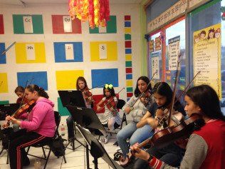 A group of young girls are playing violins in a classroom