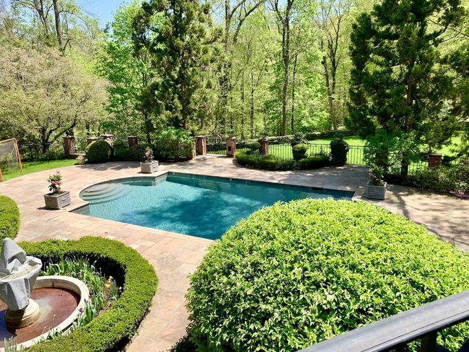 a large swimming pool surrounded by bushes and trees in a backyard .