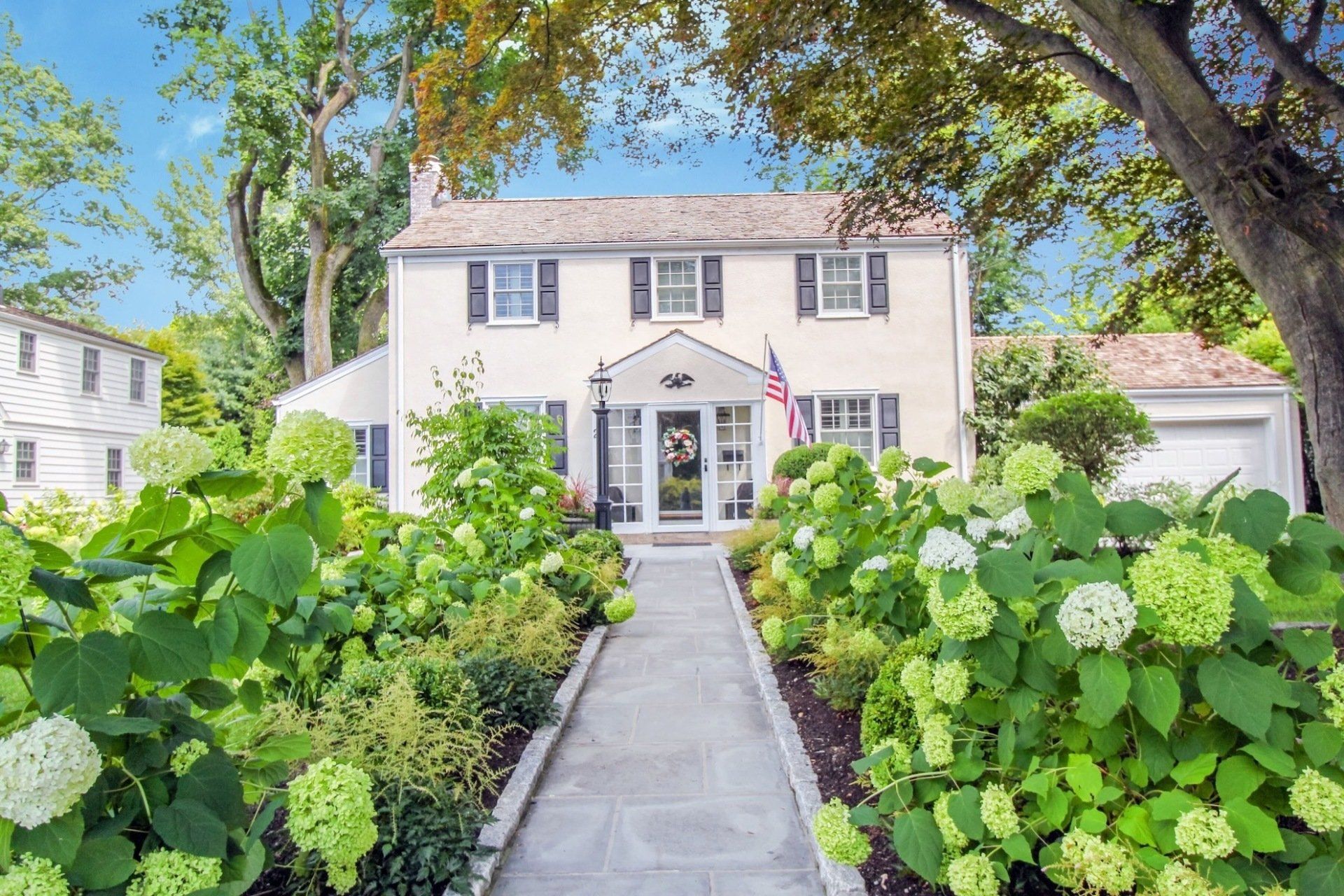 a white house with a walkway leading to it surrounded by flowers and trees .