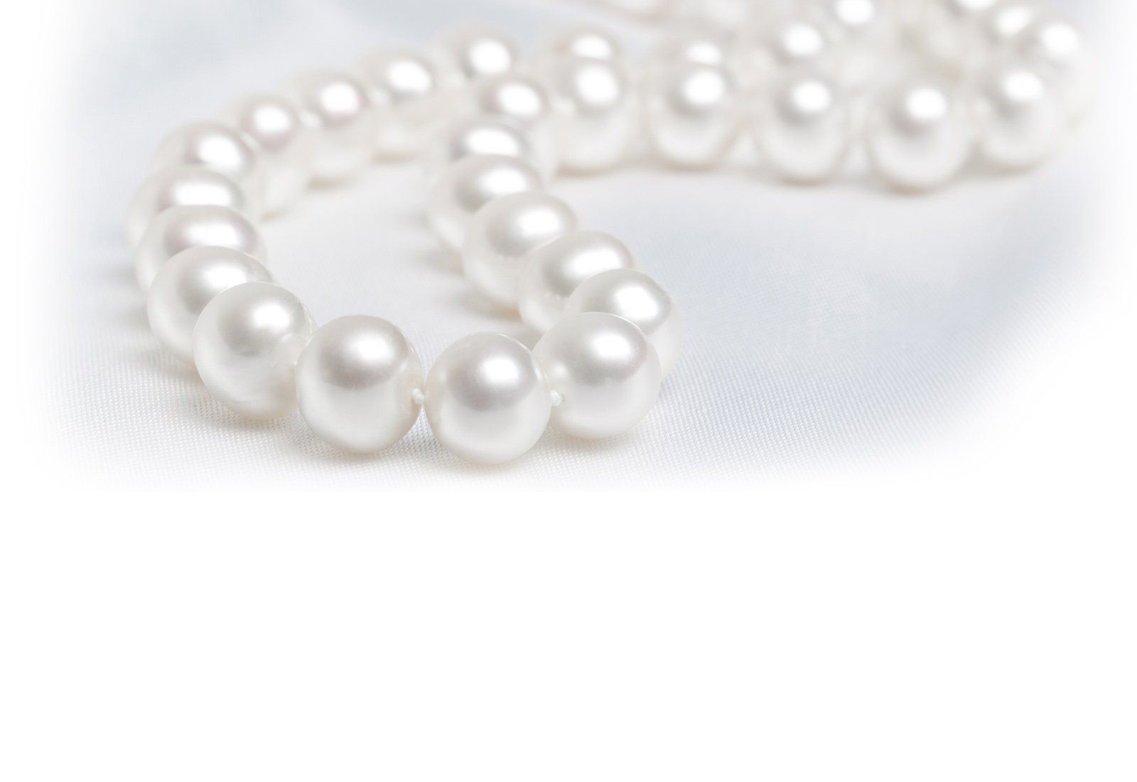 White pearl necklace on white fabric.