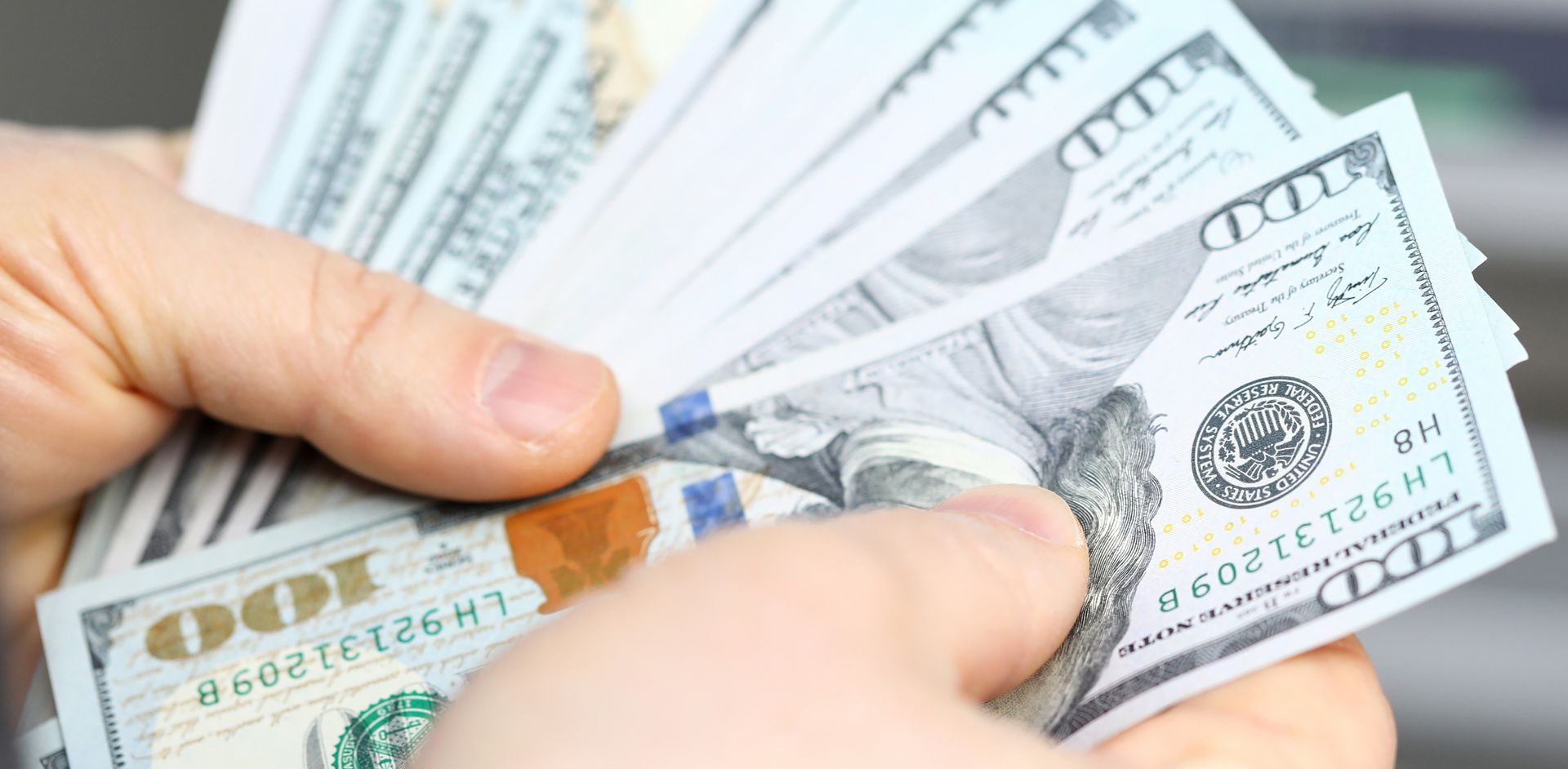 Male hands presenting a spread of hundred-dollar bills.