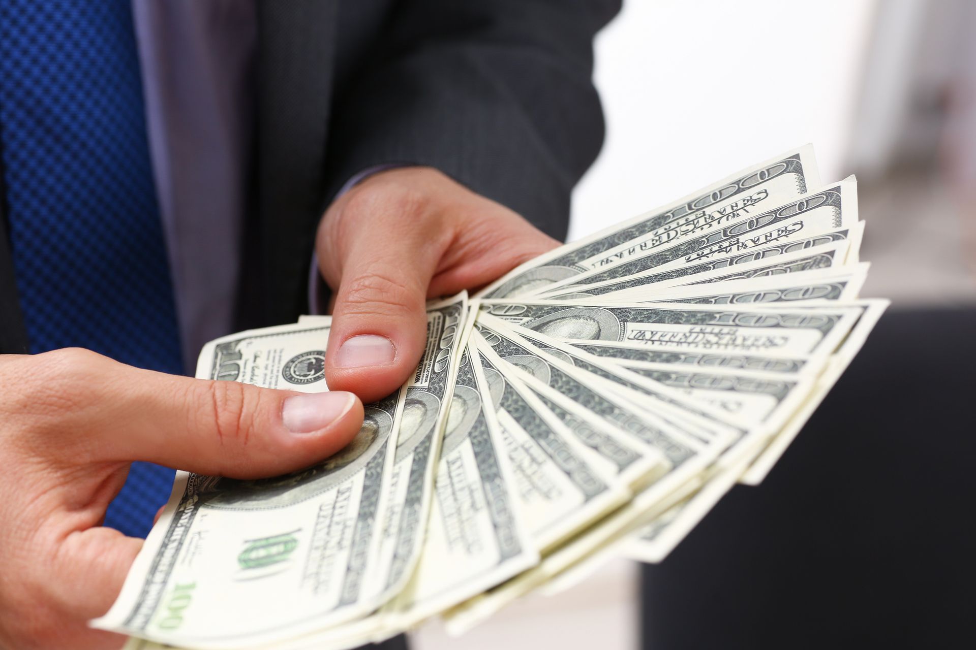 Close-up of a man in a suit holding a pack of hundred dollar bills, showcasing instant cash loans.