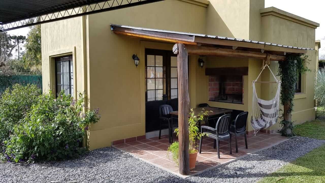 Pequeño patio amarillo con toldo de madera, sillas y una hamaca colgante en el jardín delantero.