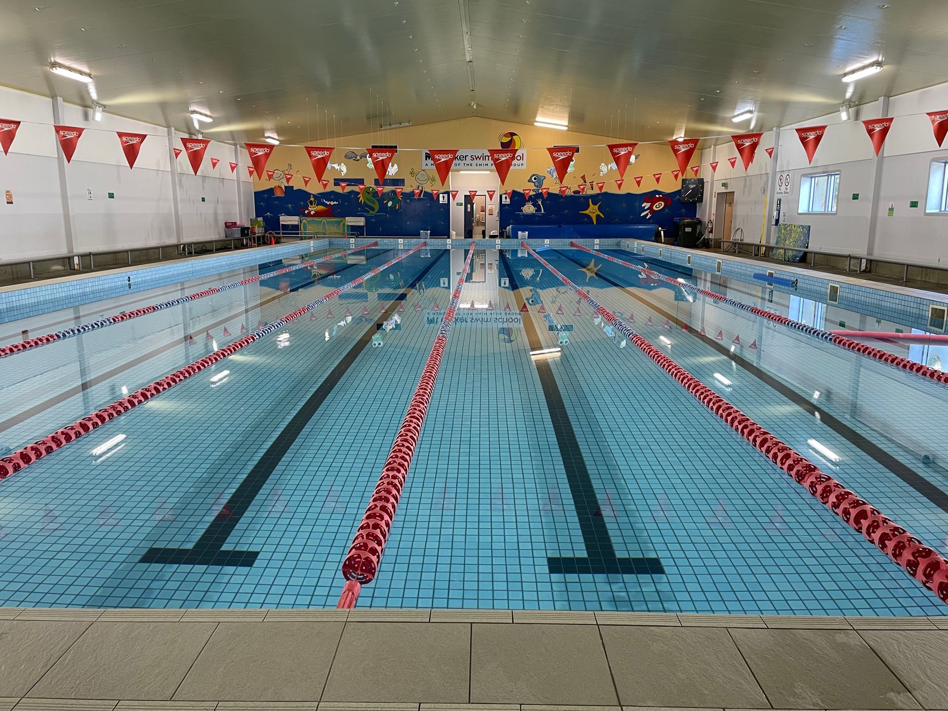 A large indoor swimming pool with red lanes and flags hanging from the ceiling.