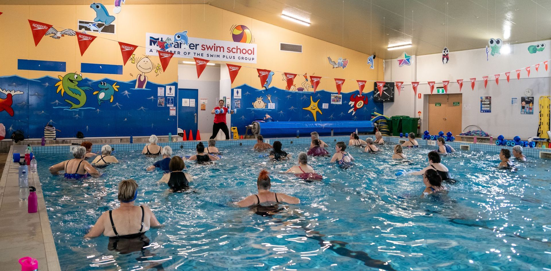 A group of people are swimming in a large indoor swimming pool.