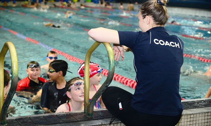 A woman is sitting on the edge of a swimming pool talking to a group of children.