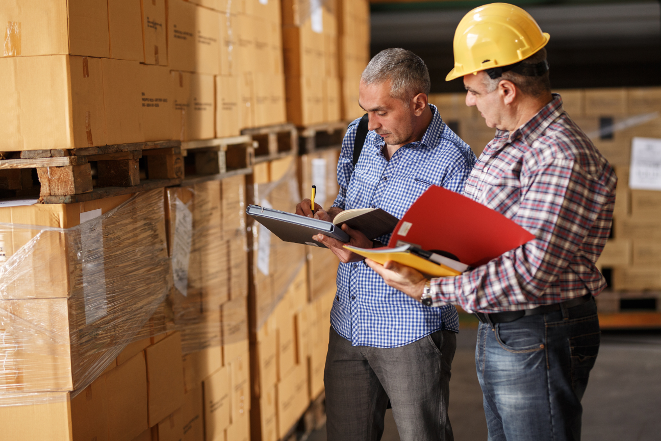 Two men are looking at a clipboard in a warehouse.