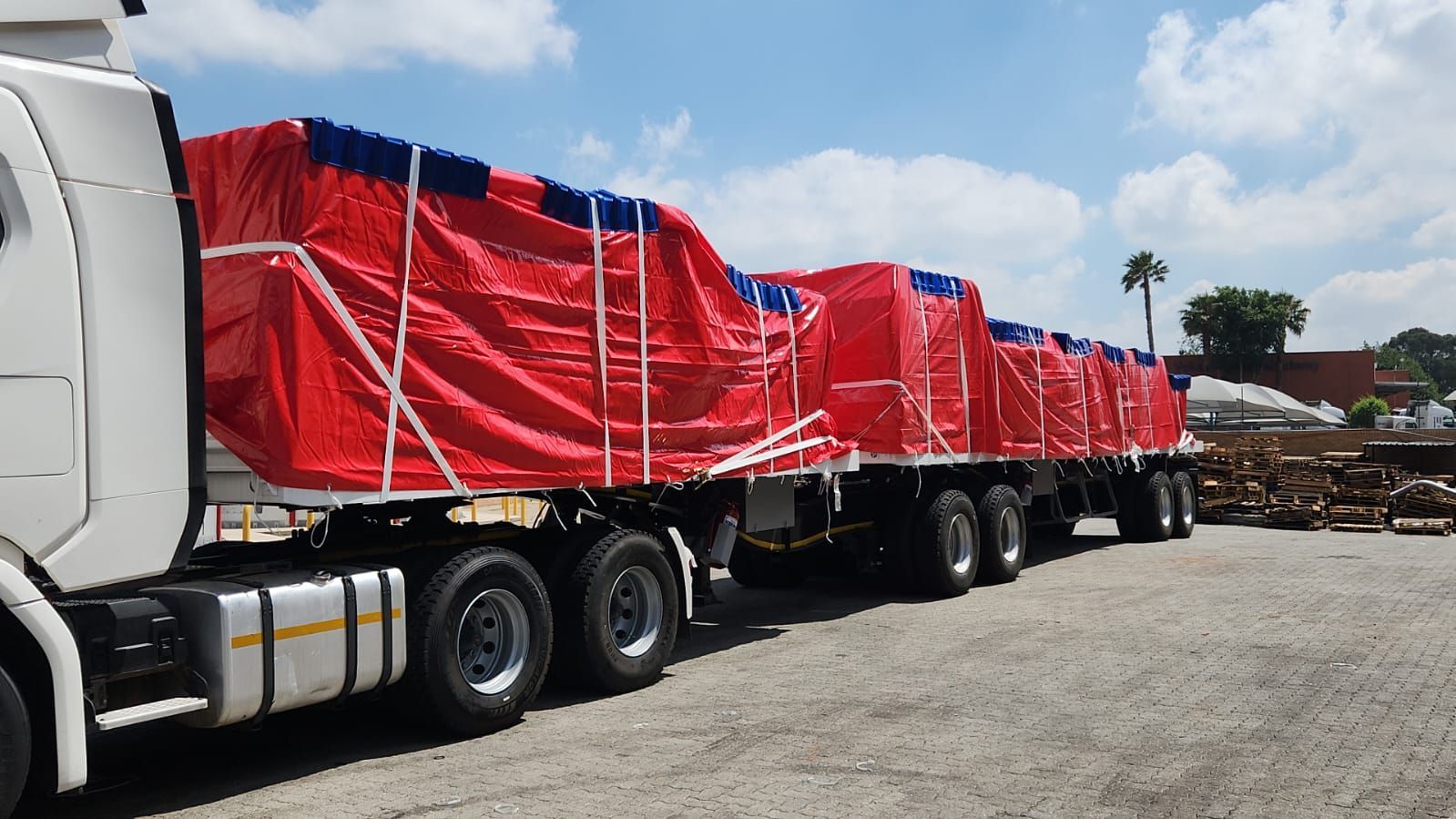 A white semi truck with a red tarp on the back is parked in a parking lot.