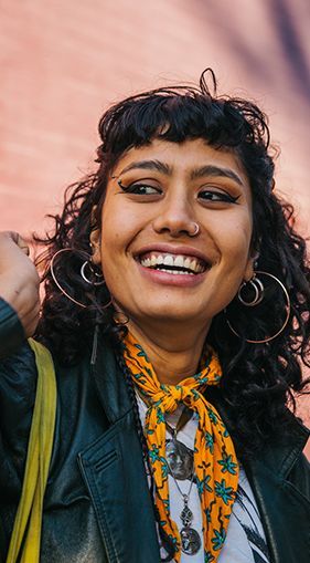 A woman wearing a scarf and hoop earrings is smiling.