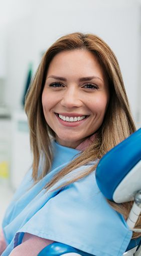 A woman is smiling while sitting in a dental chair.