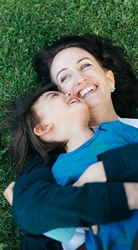 A woman and a child are laying in the grass and hugging each other.