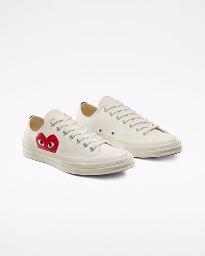Cream-colored Converse sneakers, with the red heart logo, sitting on a white surface.