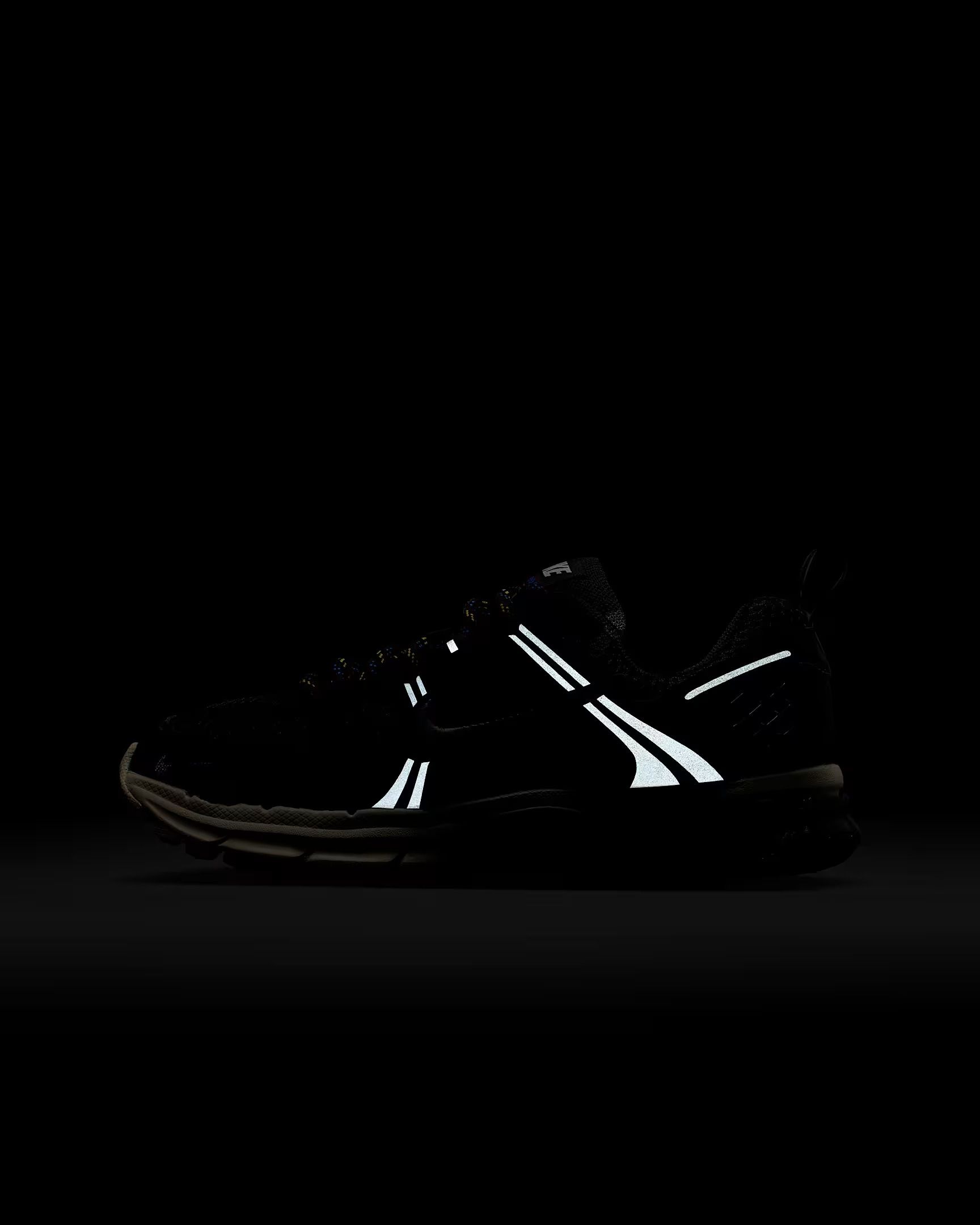 Black running shoe with reflective white accents in low light.