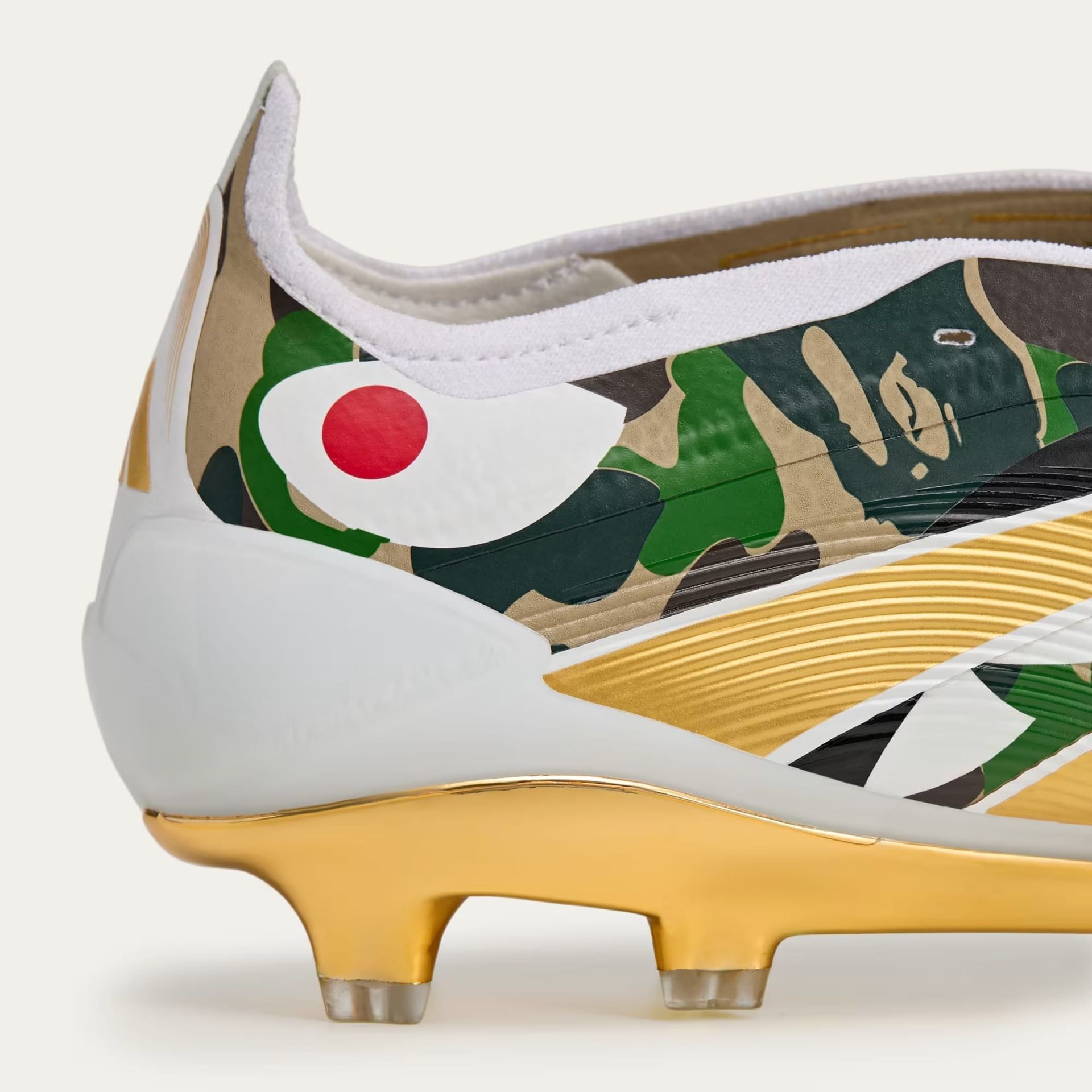 White and gold Reebok soccer cleat with a green and brown camouflage pattern and a red and white Japanese design.