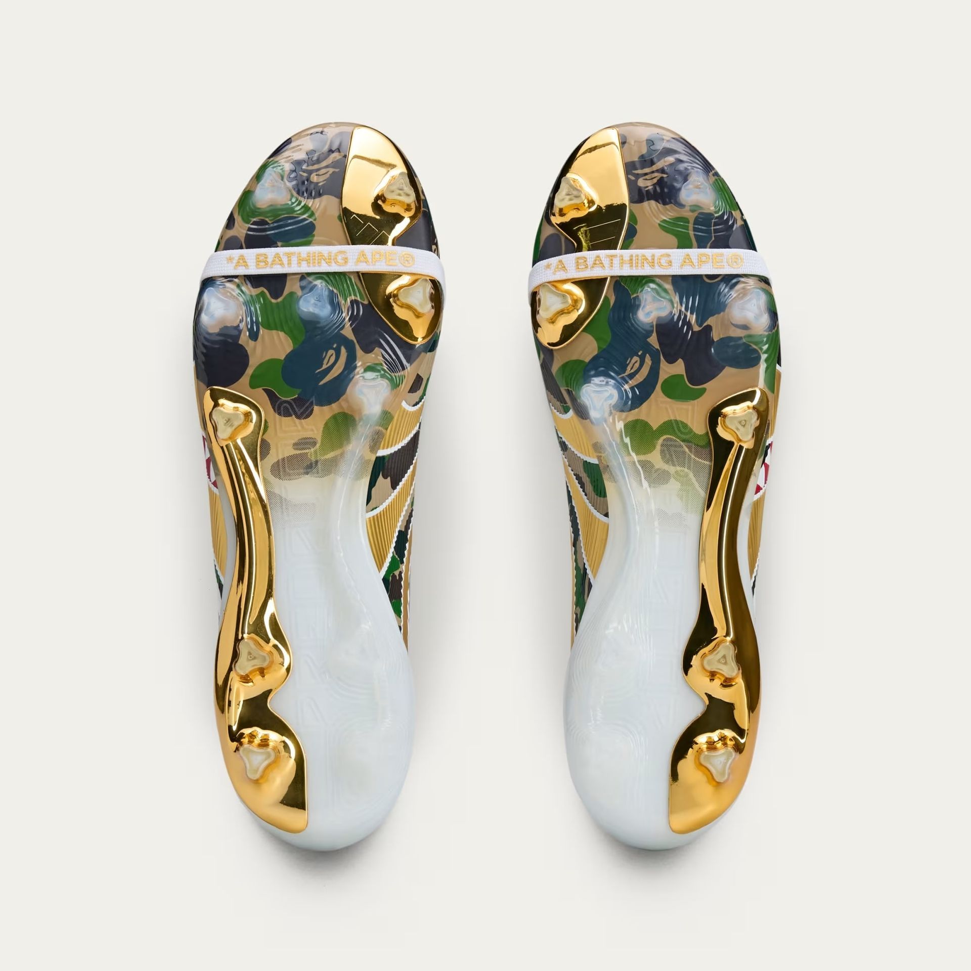 Pair of gold and camouflage BAPE shoes, seen from the soles up.