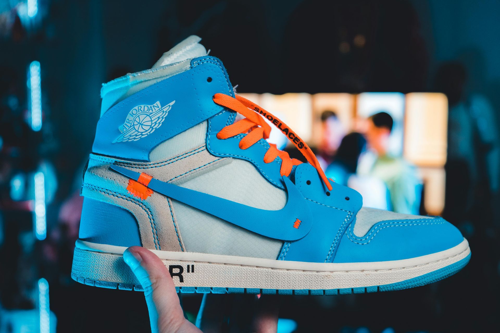 A person is holding a pair of blue and white sneakers with orange laces.