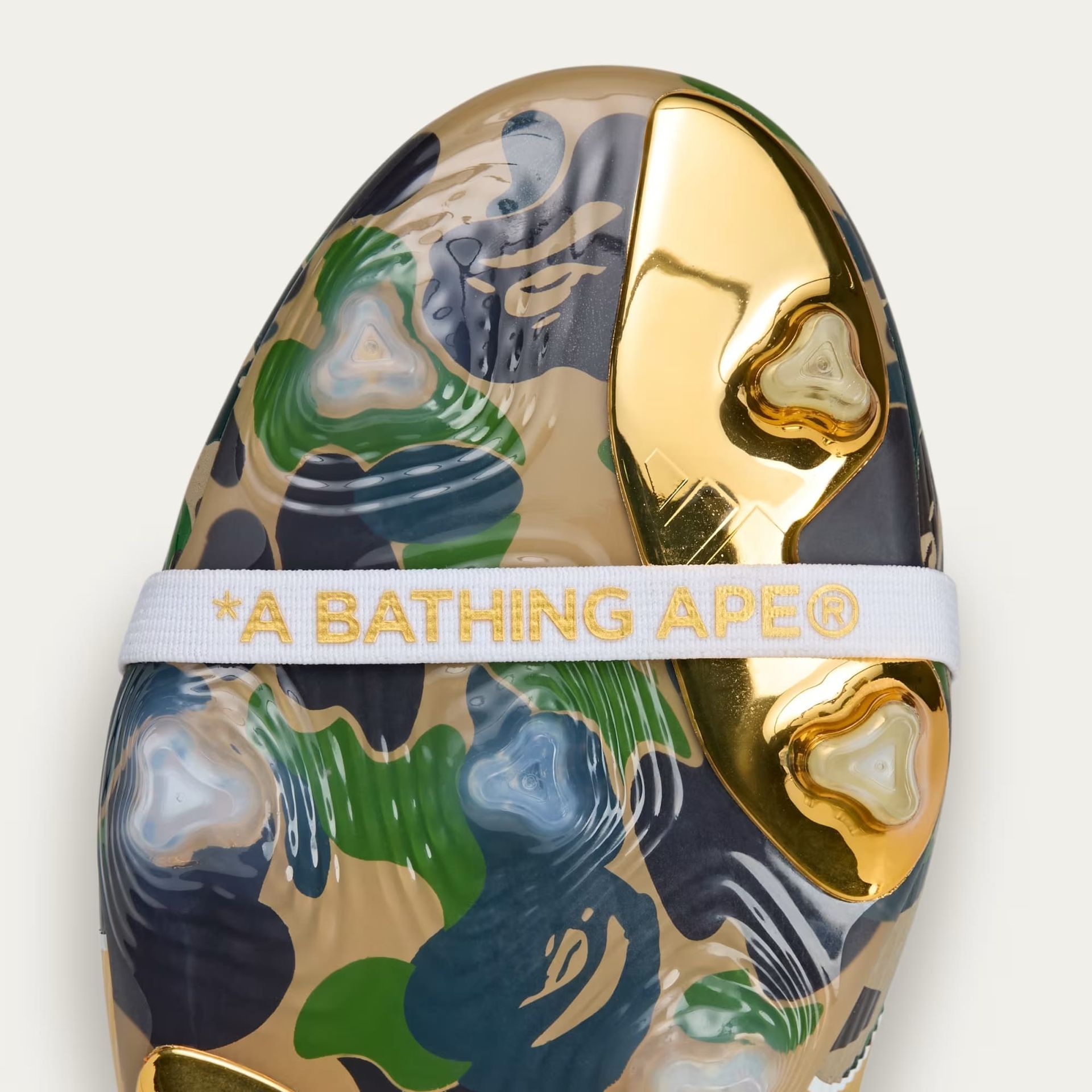 BAPE camo Crocs with gold accents and a white strap that says 