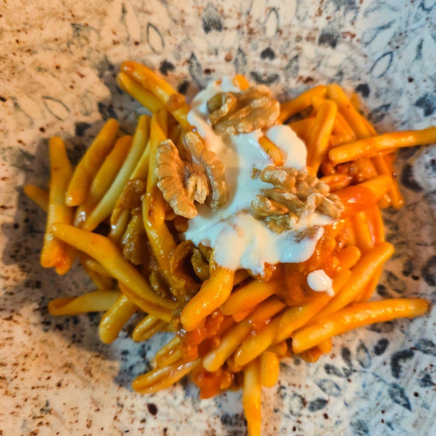Pasta con cremosa salsa bianca su un piatto maculato, mescolata con salsa all'arancia e cosparsa di pangrattato.