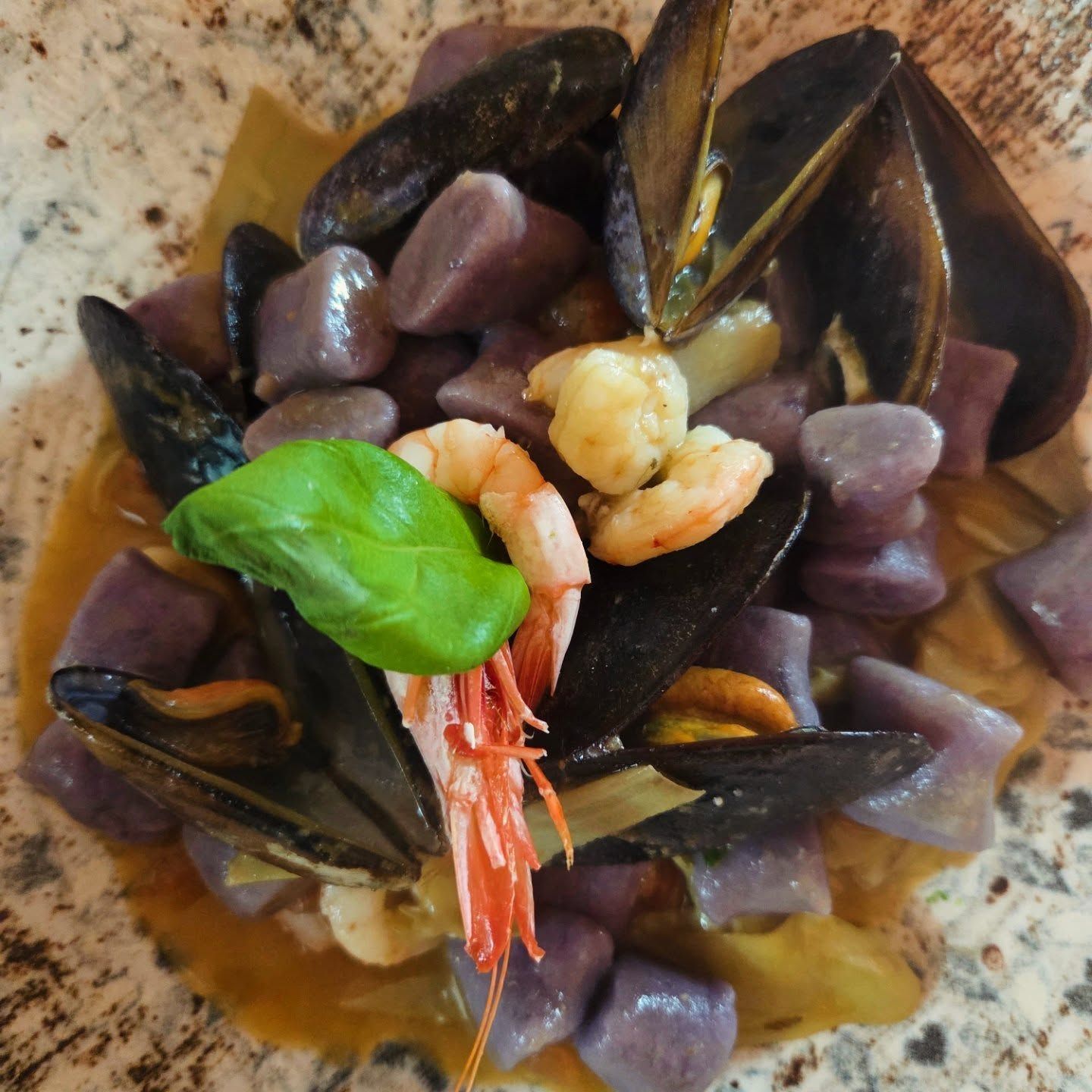 Pasta ai frutti di mare con gamberi, cozze e gnocchi viola, condita con basilico e salsa cremosa.