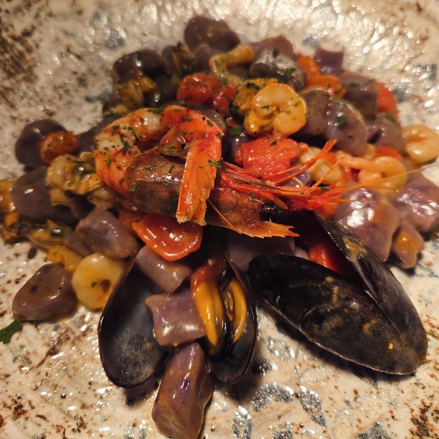 Pasta ai frutti di mare con cozze, gamberi e vongole in un sugo leggero, guarnita con erbe aromatiche e servita su un piatto punteggiato.