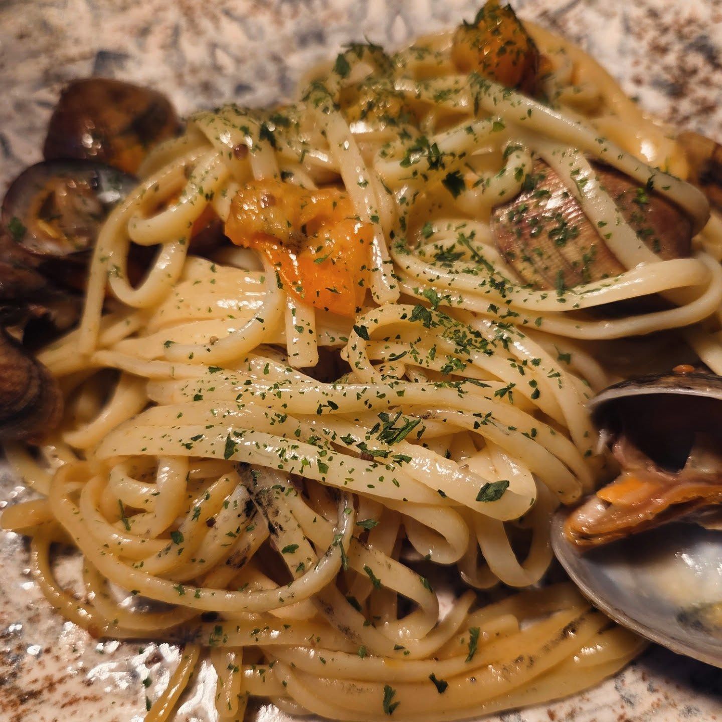 Primo piano di una cremosa pasta con vongole ed erbe aromatiche su un piatto.