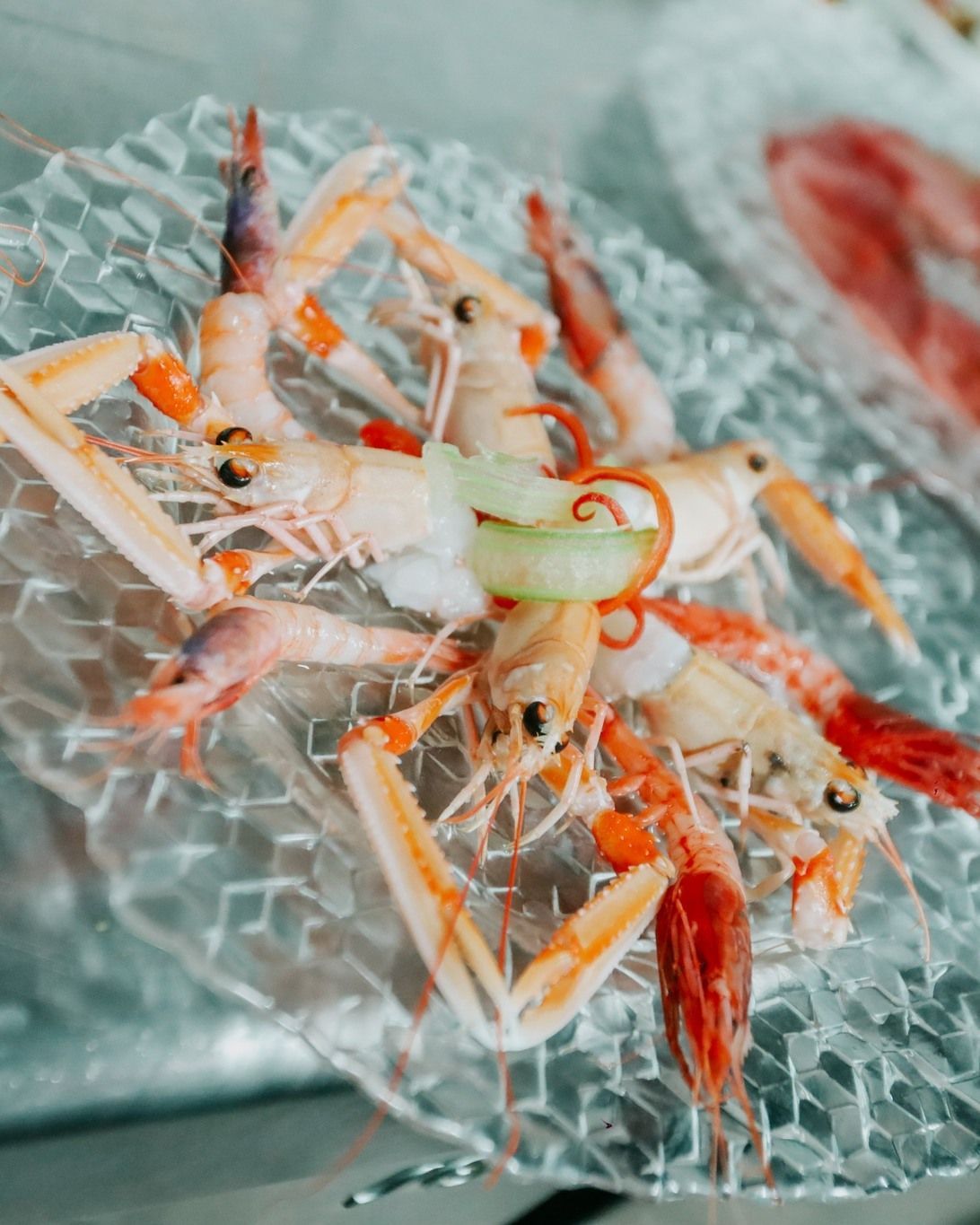Piatto di frutti di mare con gamberi e granchio su ghiaccio tritato, guarnito con fette di limone ed erbe aromatiche.