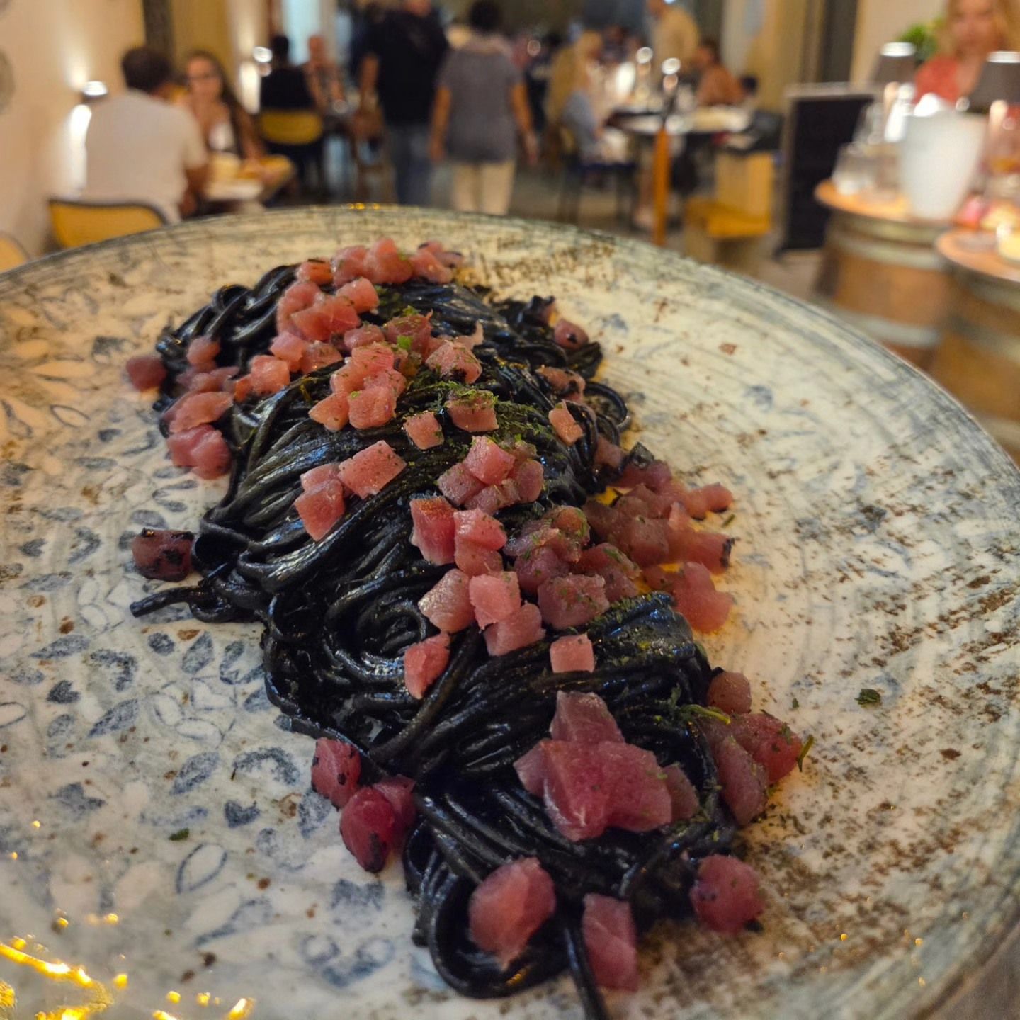 Pasta al nero di seppia con prosciutto rosa a dadini su un piatto maculato in un ristorante