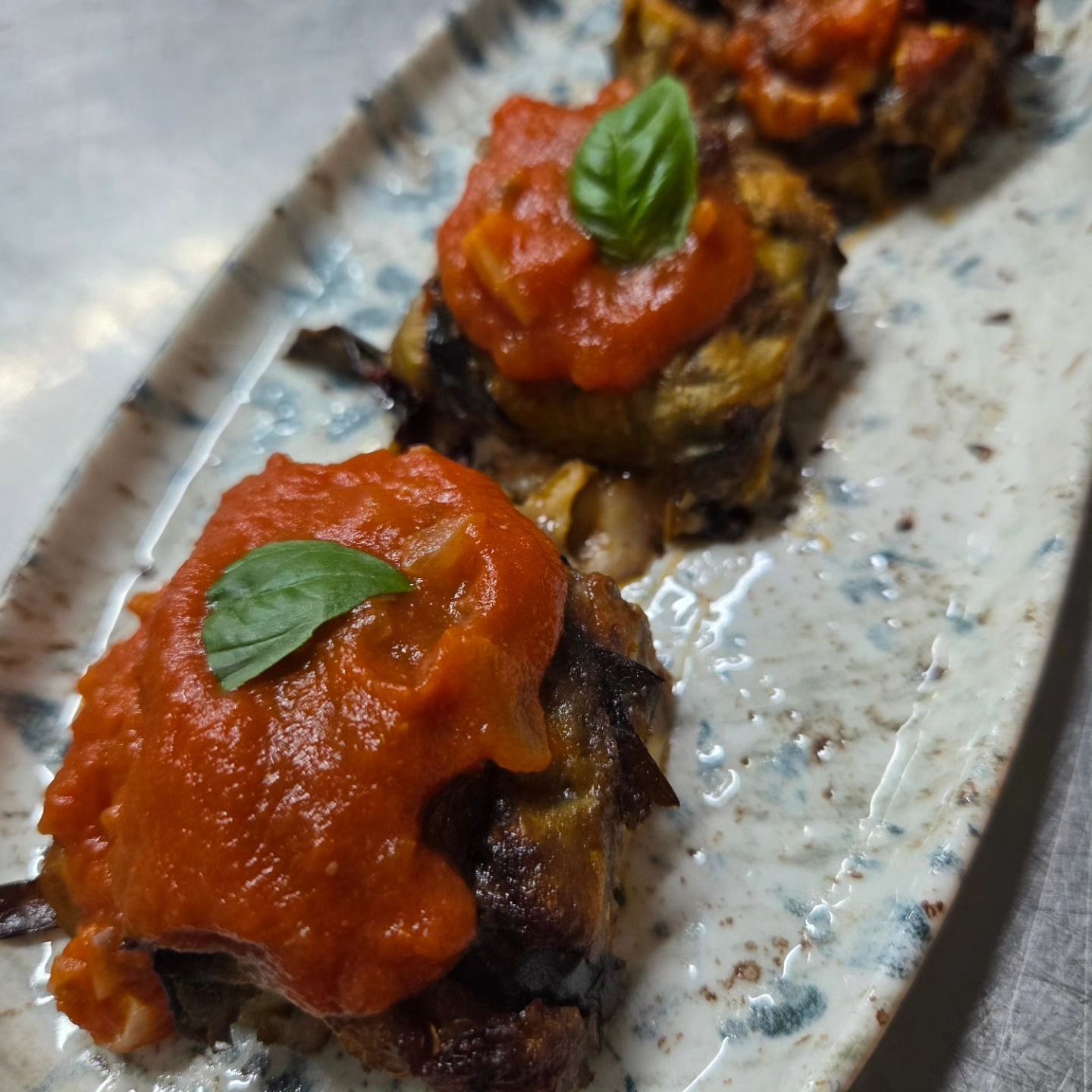 Tre bocconcini di pane tostato con pomodoro e basilico, serviti su un piatto maculato.