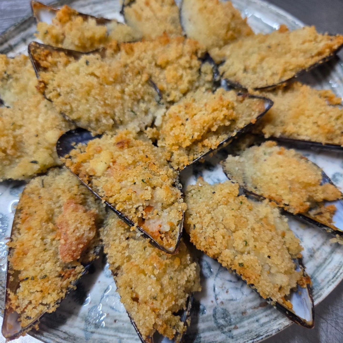Cozze al forno ricoperte di pangrattato dorato, disposte su un vassoio.