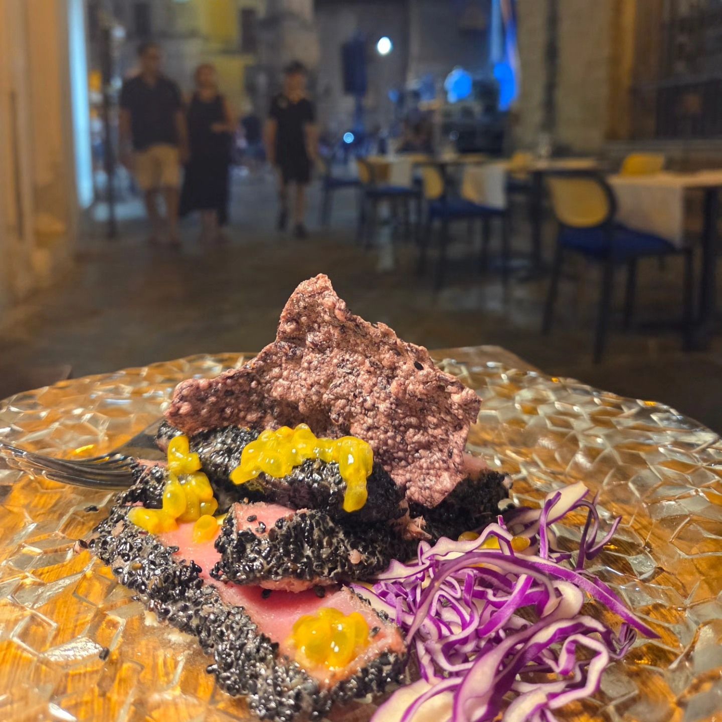 Piatto gourmet con insalata di cavolo viola su un tavolo di vetro in un ristorante dalle luci soffuse.
