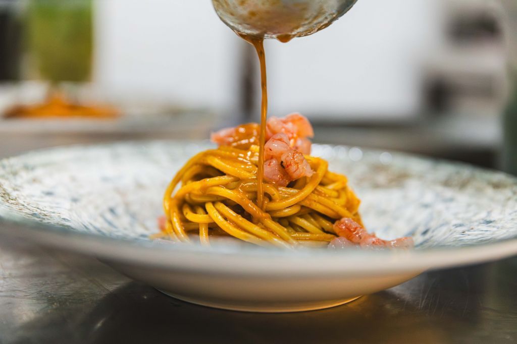 Spaghetti in una ciotola bianca, conditi con la salsa servita con un cucchiaio.